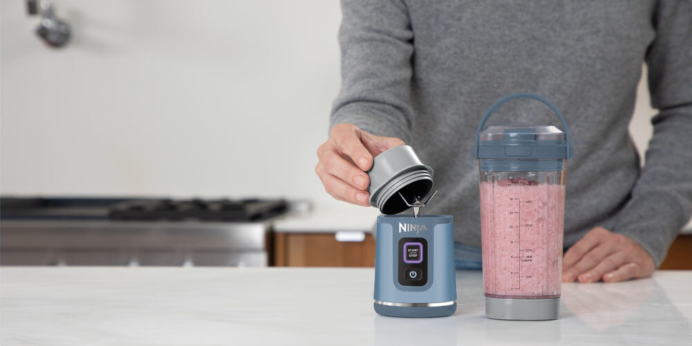 Blender personalny NINJA Blast BC151EUNV Niebieski Bezprzewodowy stoi na blacie pojemnik z napojem wewnątrz osoba otwiera podstawę blendera z ostrzami przycisk na obudowie kubek pokrywka wolne od BPA dla zdrowego i wygodnego gotowania możliwość mycia w zmywarce funkcja samoczyszczenia woda kropla płynu do naczyń 30 sekundowy cykl miksowania płukanie dla bezpieczeństwo ostrzy zakładanie pokrywy ochronne