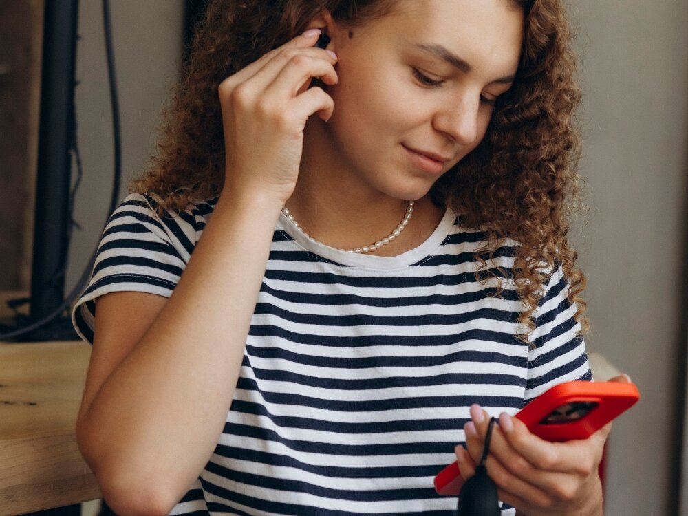 Słuchawki dokanałowe CANYON TWS-5 kobieta z sluchawka w uchu i smartfonem w rece, polaczenia telefoniczne rozmowy mikrofony