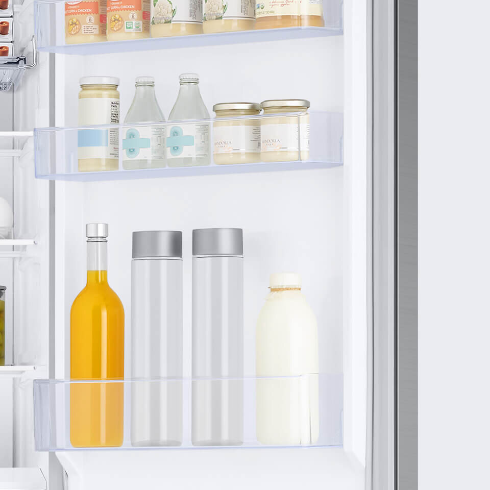 Wnętrze lodówki z trzema półkami na drzwiach, na których znajdują się różne produkty spożywcze, w tym butelki i słoiki. Produkty są uporządkowane, a wnętrze lodówki jest jasne i przestronne.