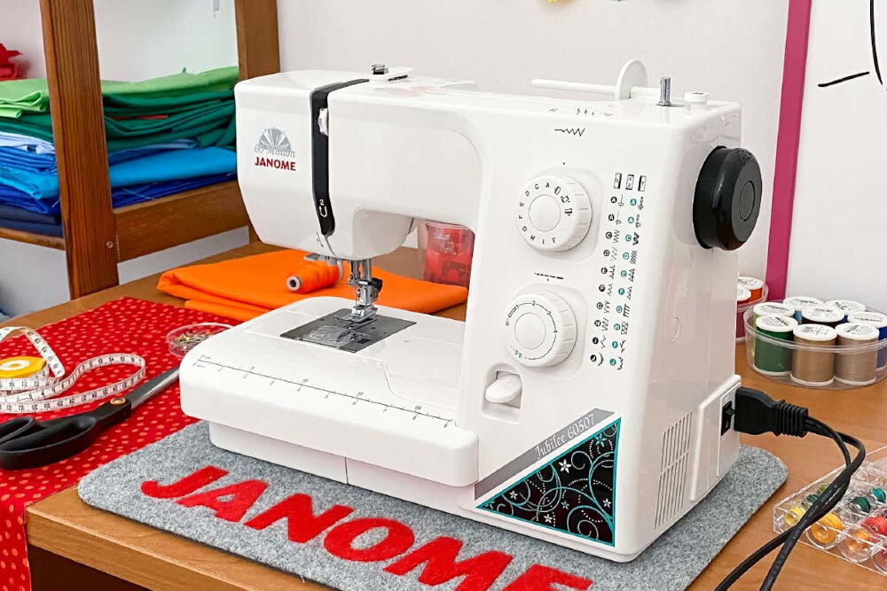 Maszyna do szycia JANOME Jubilee 60507 maszyna stojąca bokiem biała czarne elementy pokrętła zasilanie materiał z tyłu różne kolory nici jakość trwałość solidna metalowa konstrukcja metalowe podzespoły stabilność podczas szycia długa żywotność solidne maszyny do szycia w rękach początkujących bardziej zaawansowanych użytkowników