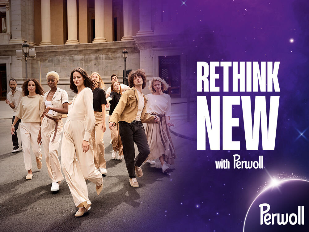 Grupa uśmiechniętych, modnie ubranych młodych ludzi maszeruje ulicą na tle starożytnych kolumn. Hasło: RETHINK NEW with Perwoll na tle kosmicznej, fioletowej grafiki. Obraz promuje nowe podejście do odzieży.