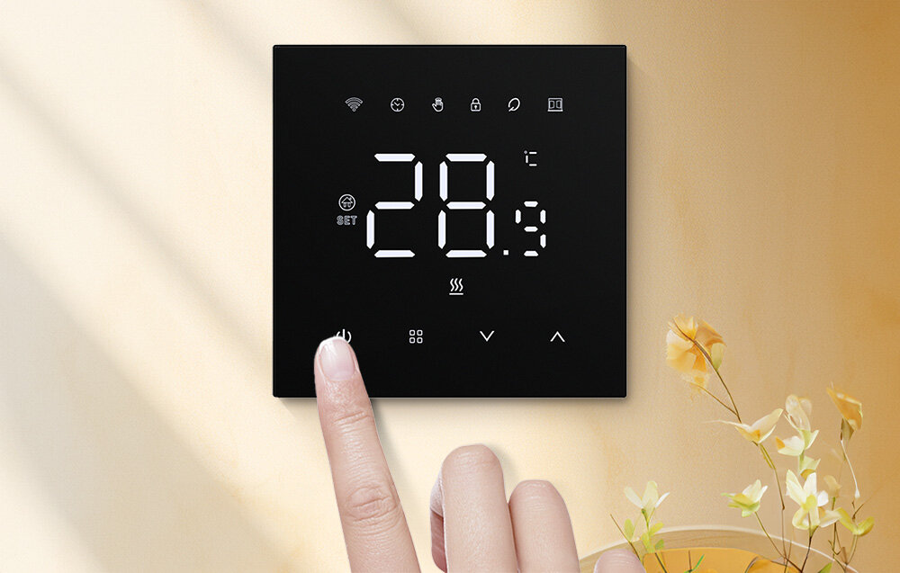 Czarny panel z wyświetlaczem pokazującym temperaturę 28,9°C oraz ikonami wskazującymi różne funkcje. Palec dotyka przycisku na panelu, a w tle widać delikatne kwiaty.