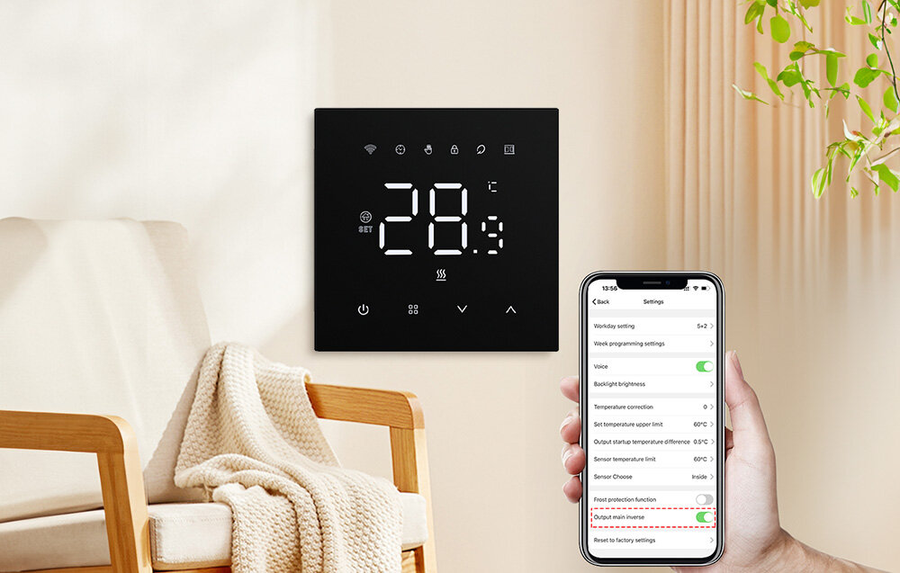 Na ścianie wisi czarny panel z wyświetlaczem pokazującym temperaturę 28,9°C oraz ikonami. Obok osoba trzyma smartfon z aplikacją do sterowania ustawieniami termostatu.