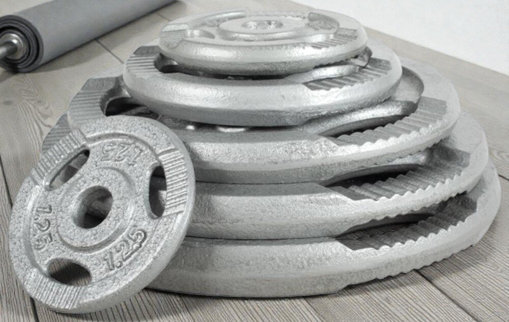 Obciążenie GORILLA SPORTS Grip (15 kg) drewniana podłoga zestaw obciążeń ustawionych jedno na drugim w tle leży szara rolka specjalne, trzy ergonomiczne uchwyty wygodne przenoszenie i szybkie zakładanie krążków na gryf jak hantli zwiększa liczbę zastosowań jednego elementu ogranicza ślizganie dłoni poprawia kontrolę ruchu