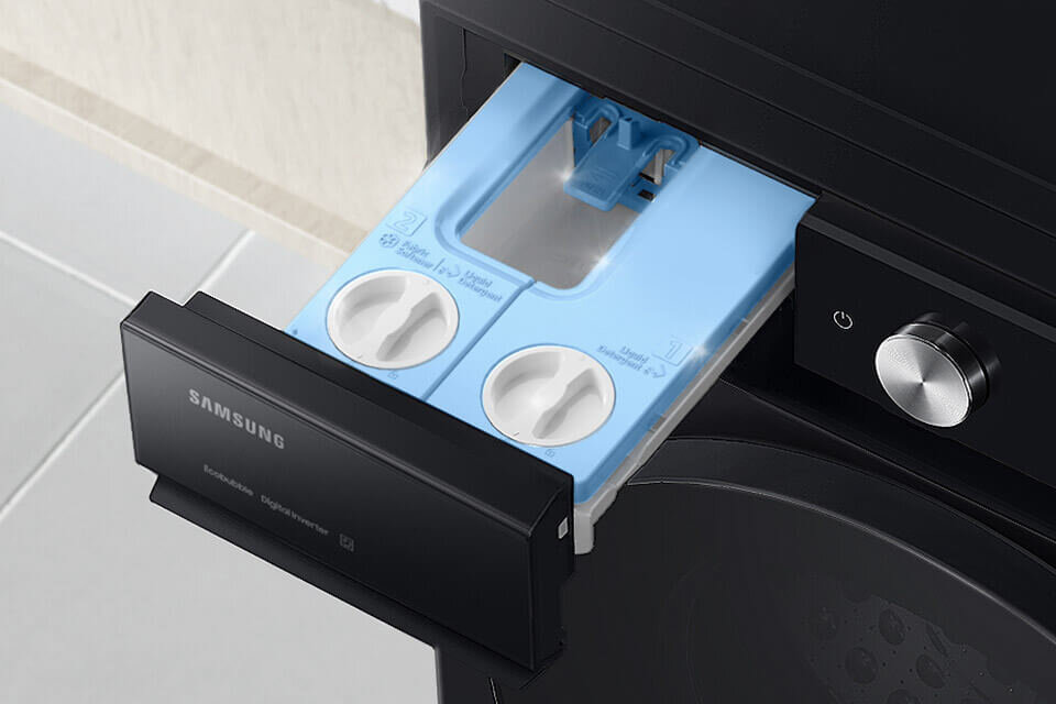 Obraz przedstawia otwarty dozownik pralki z dwoma komorami na detergent, w kolorze niebieskim. Na froncie dozownika widoczne jest logo \'SAMSUNG\' oraz napisy \'Ecobubble\' i \'Digital Inverter\'.