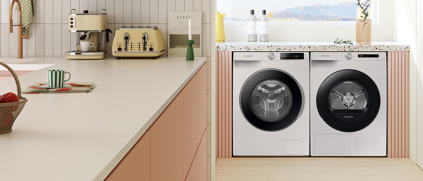 Na obrazie widoczna jest kuchnia z kremowym ekspresem do kawy i tosterem na blacie oraz pralka i suszarka marki Samsung w zabudowie. Pralka ma napis \'Ecobubble\' na drzwiach, a suszarka \'Heatpump\'.