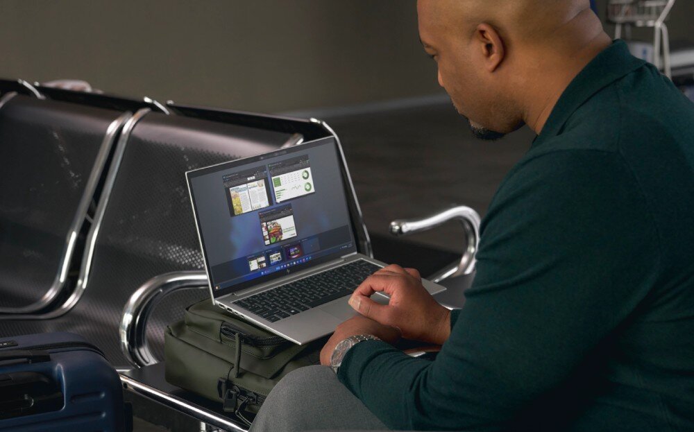 Laptop HP EliteBook 1040 G10 Mężczyzna w ciemnej bluzie siedzący w poczekalni na lotnisku, korzystający z laptopa ustawionego na torbie podróżnej. W tle metalowe krzesła i bagaże, obudowa, kolor, wytrzymałość, odporność