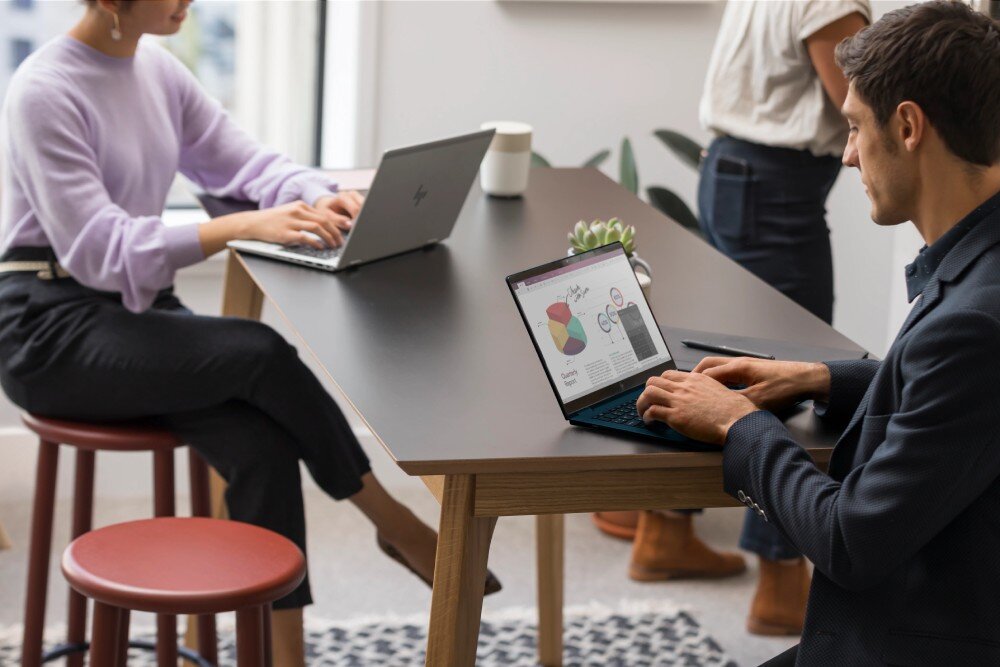 Laptop HP EliteBook 1040 G10 Mężczyzna w garniturze pracujący na laptopie przy stole w otwartej przestrzeni biurowej. W tle kobieta w liliowym swetrze również korzysta z laptopa, podzespoły, procesor, karta graficzna, pamięć RAM