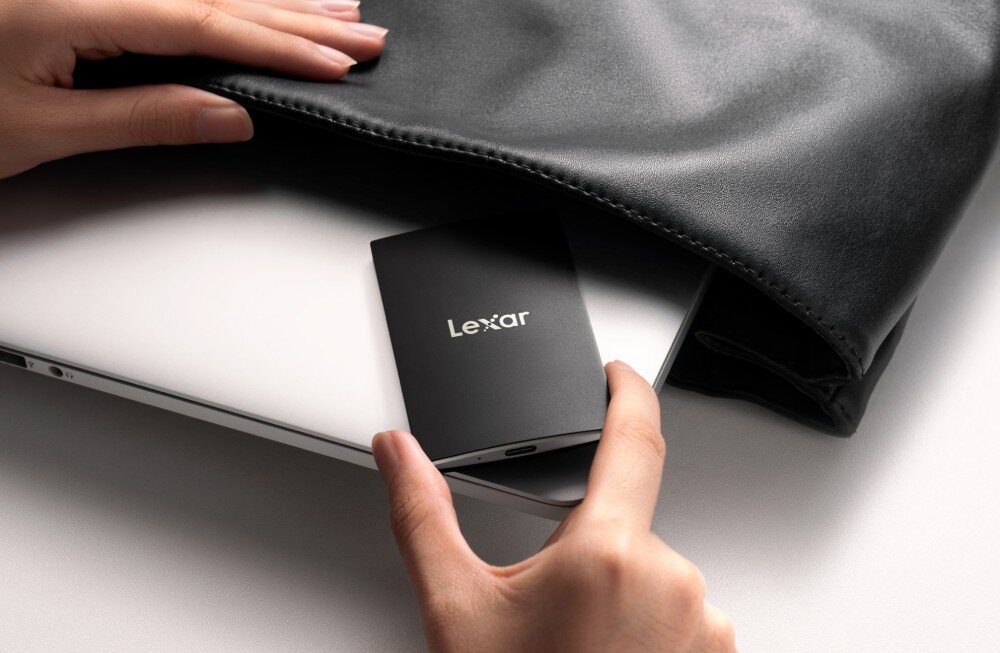 Dysk LEXAR SL500 Dłonie wsuwające smukły czarny dysk do kieszeni w skórzanej torbie leżącej obok zamkniętego laptopa