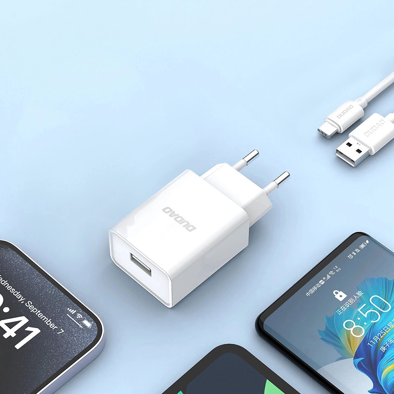 Na obrazie widoczna jest biała ładowarka sieciowa z logo \'DUDAO\' oraz kabel USB-A do USB-C. W tle znajdują się fragmenty smartfonów na jasnoniebieskim tle.