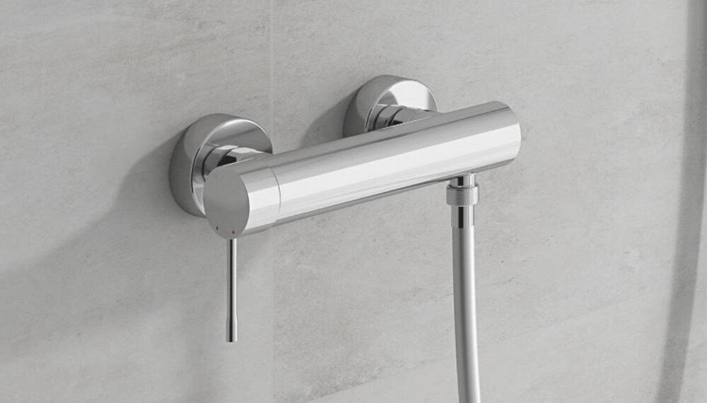 BATERIA PRYSZNICOWA GROHE ESSENCE 33636001 CHROM Na zdjęciu widoczna jest natynkowa bateria prysznicowa o cylindrycznym kształcie, zamontowana na jasnej, gładkiej ścianie. Chromowane wykończenie nadaje jej elegancki wygląd