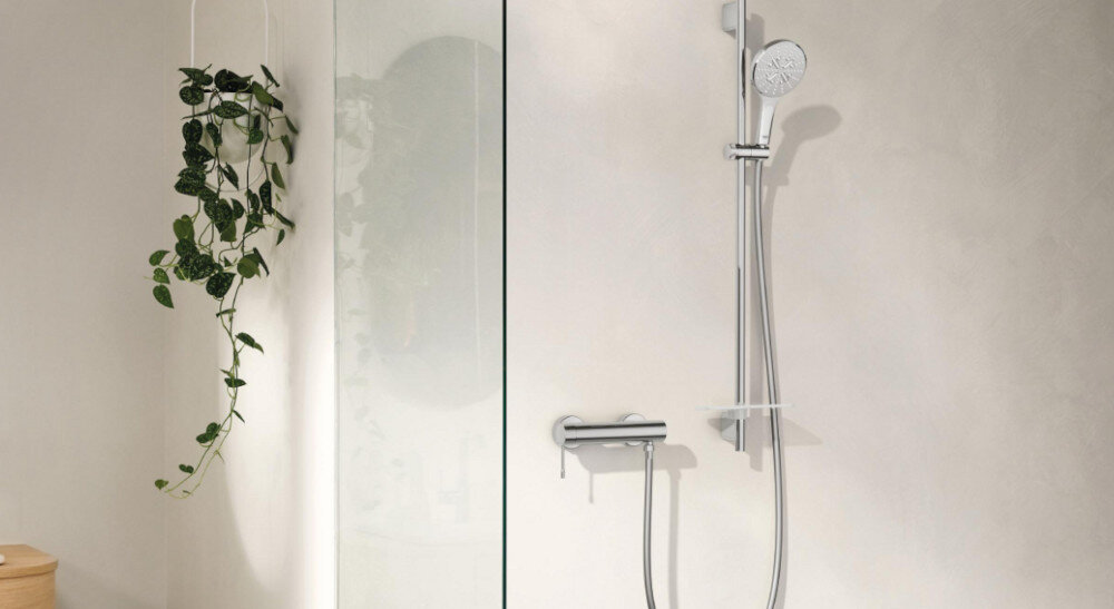 BATERIA PRYSZNICOWA GROHE ESSENCE 33636001 CHROM Przedstawiono kompletną strefę prysznicową z baterią, słuchawką prysznicową na drążku oraz szklaną ścianką. Jasna aranżacja z dodatkiem rośliny podkreśla minimalistyczny charakter wnętrza montaż ścienny armatura łazienkowa elegancki design trwałe wykonanie