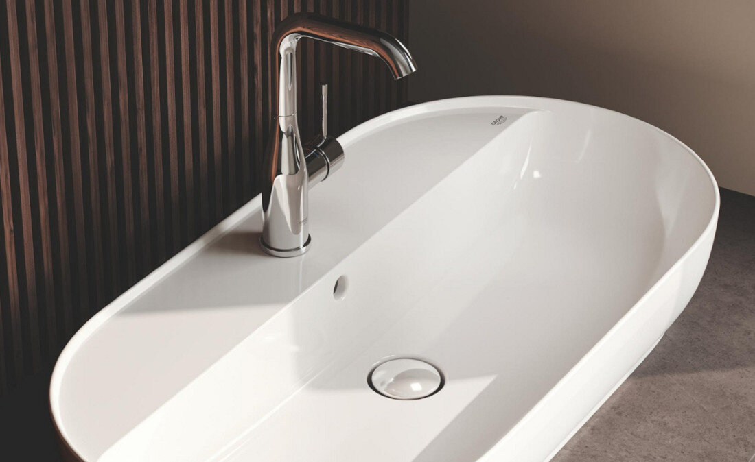 BATERIA UMYWALKOWA GROHE ESSENCE ROZMIAR L 23541001 CHROM Na zdjęciu przedstawiono elegancką, chromowaną baterię umywalkową zamontowaną na dużej, białej umywalce o nowoczesnym, opływowym kształcie. Tło z pionowych, drewnianych paneli dodaje aranżacji ciepła i kontrastuje z minimalistycznym stylem armatury elegancki design chrom Long-Life lustrzany blask odporność uszkodzenia łatwe czyszczenie stylowe wzornictwo