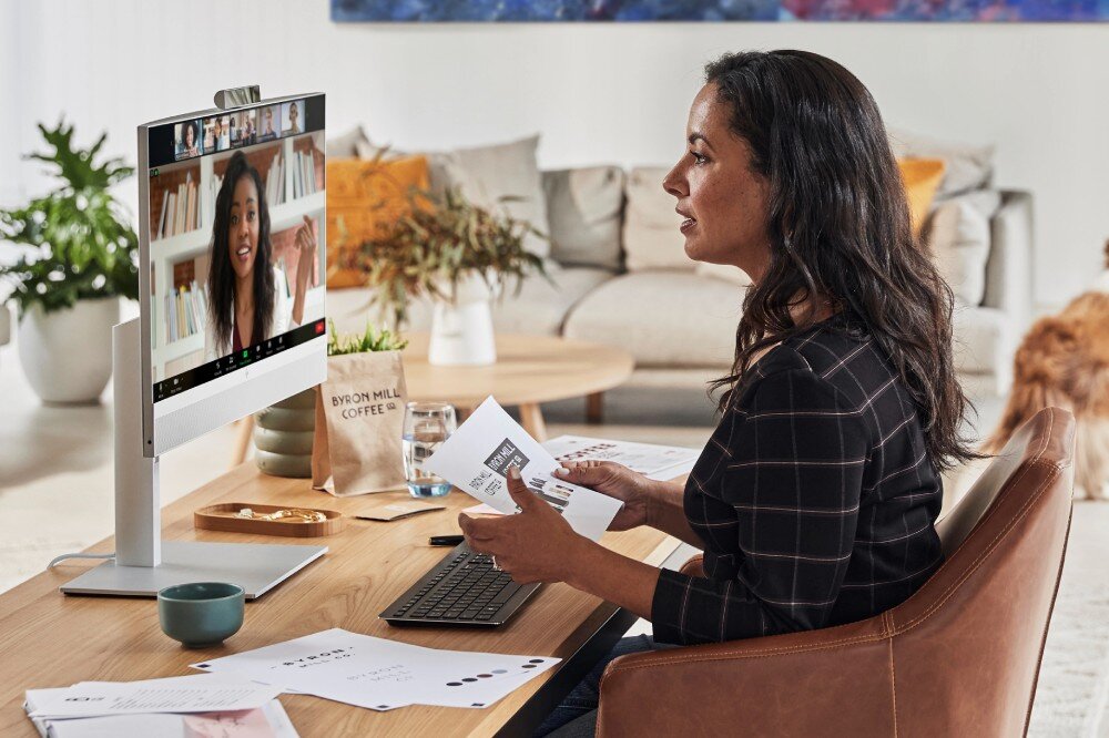 Komputer HP EliteOne 840 G9 Kobieta siedzi przy biurku w domowym wnętrzu i uczestniczy w wideokonferencji na komputerze typu All-in-One, trzyma w rękach wydrukowane materiały, przekątna, matryca, przeznaczenie