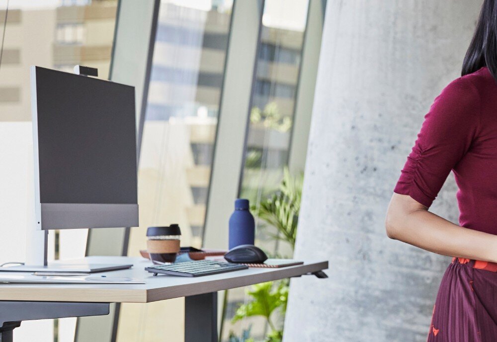 Komputer HP EliteOne 840 G9 Biurko z komputerem typu All-in-One, klawiaturą i kubkiem wielokrotnego użytku, na tle przeszklonego biura, zabezpieczenia, funkcje