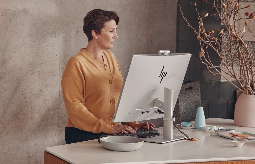 Komputer HP EliteOne 870 G9 Kobieta siedzi przy komputerze w zabudowanej wnęce biurowej, obok niej mężczyzna na fotelu i pies na dywanie, wyświetlacz, rozdzielczość, matryca