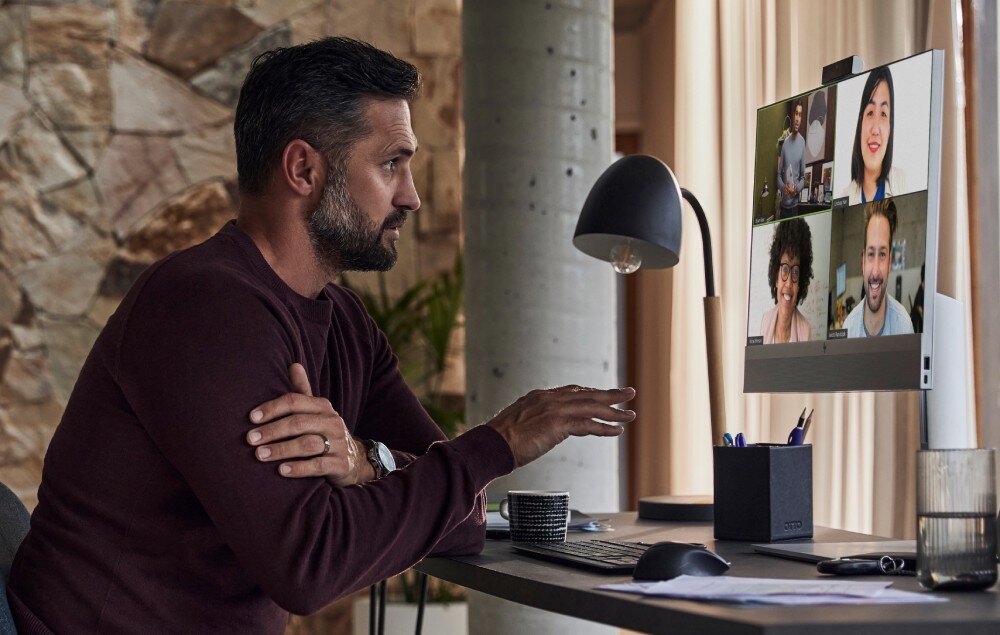 Komputer HP EliteOne 840 G9 Mężczyzna z brodą prowadzi rozmowę wideo na komputerze typu All-in-One, w tle jasny pokój z kamienną ścianą i zasłonami, procesor, rdzenie, pamięć, dysk