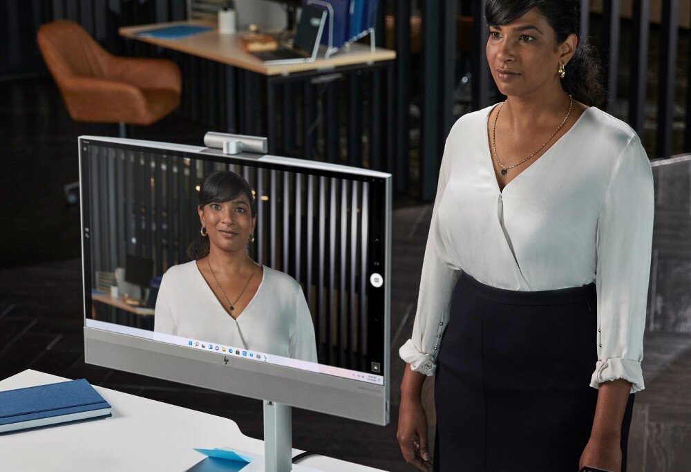 Komputer HP EliteOne 840 G9 Kobieta stoi naprzeciw komputera typu All-in-One, na ekranie widoczny jest jej wizerunek z kamery, rozdzielczość, ekran dotykowy, kamera, mikrofon, głośniki