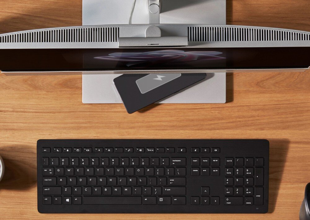 Komputer HP EliteOne 840 G9 Widok z góry na komputer typu All-in-One, klawiaturę i stojący na podstawie telefon z ikoną ładowania, obudowa, kolor, porty, gniazda