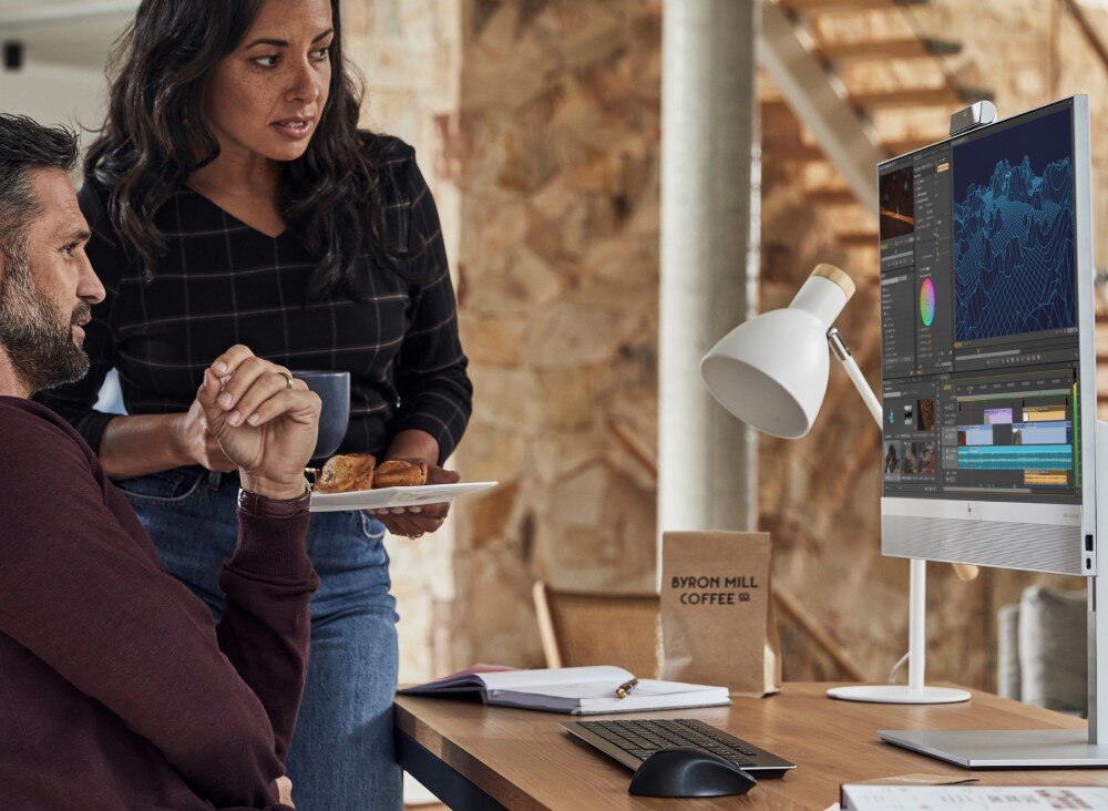 Komputer HP EliteOne 870 G9 Mężczyzna i kobieta rozmawiają przy biurku, na którym stoi komputer typu all-in-one z wyświetlonym programem do edycji wideo, opis