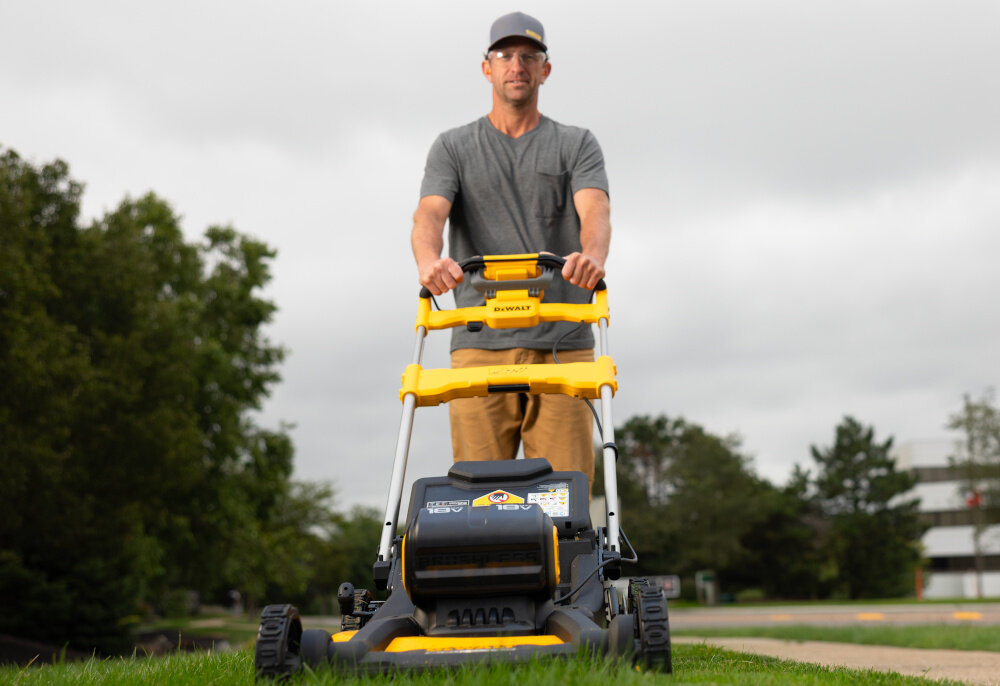 Kosiarka akumulatorowa DEWALT DCMWSP156N-XJ z napędem ogród trawnik osoba kosi trawę w ogrodzie w tle drzewa niebo zadbany trawnik koszenie trawy wygoda