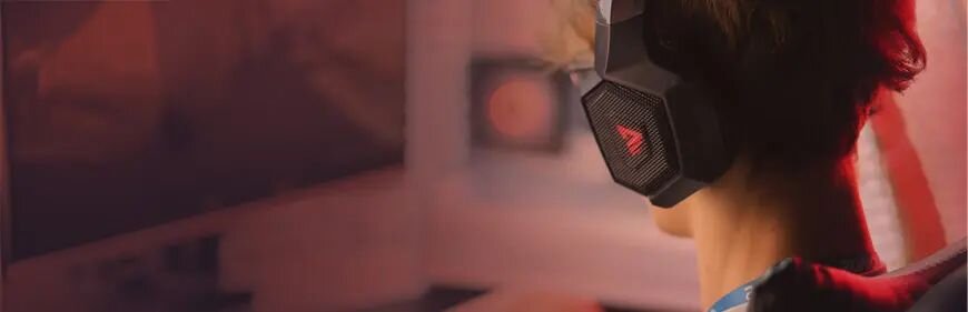 Osoba siedząca przy komputerze, na głowie słuchawki gamingowe Savio z czerwonym logo, lekko rozmyte tło.
