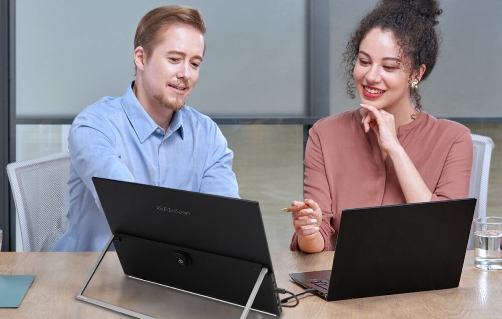 Monitor ASUS ZenScreen MB229CF Kobieta i mężczyzna siedzą przy biurku i wspólnie korzystają z laptopa oraz monitora ustawionego na składanej podstawce. Mężczyzna wskazuje coś na ekranie monitora, waga, grubość, konstrukcja, podstawka