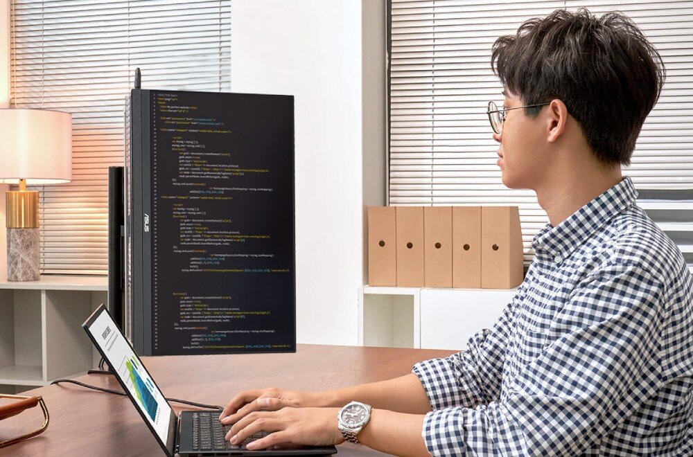 Monitor ASUS ZenScreen MB229CF Mężczyzna pracuje przy biurku z monitorem ustawionym pionowo. Na ekranie wyświetlony jest kod źródłowy. Obok laptop z otwartym dokumentem, ramię, zacisk, regulacja, szybkozłączka