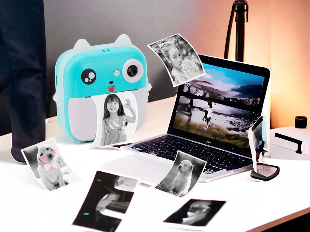 Drukarka EXTRALINK EPP-004 Złącze USB Niebieski aparat-drukarka na biurku obok laptopa, otoczony przez wydrukowane czarno-białe zdjęcia psów i ludzi wbudowany aparat połączenie z modułem drukującym eliminacja potrzeby przesyłania plików