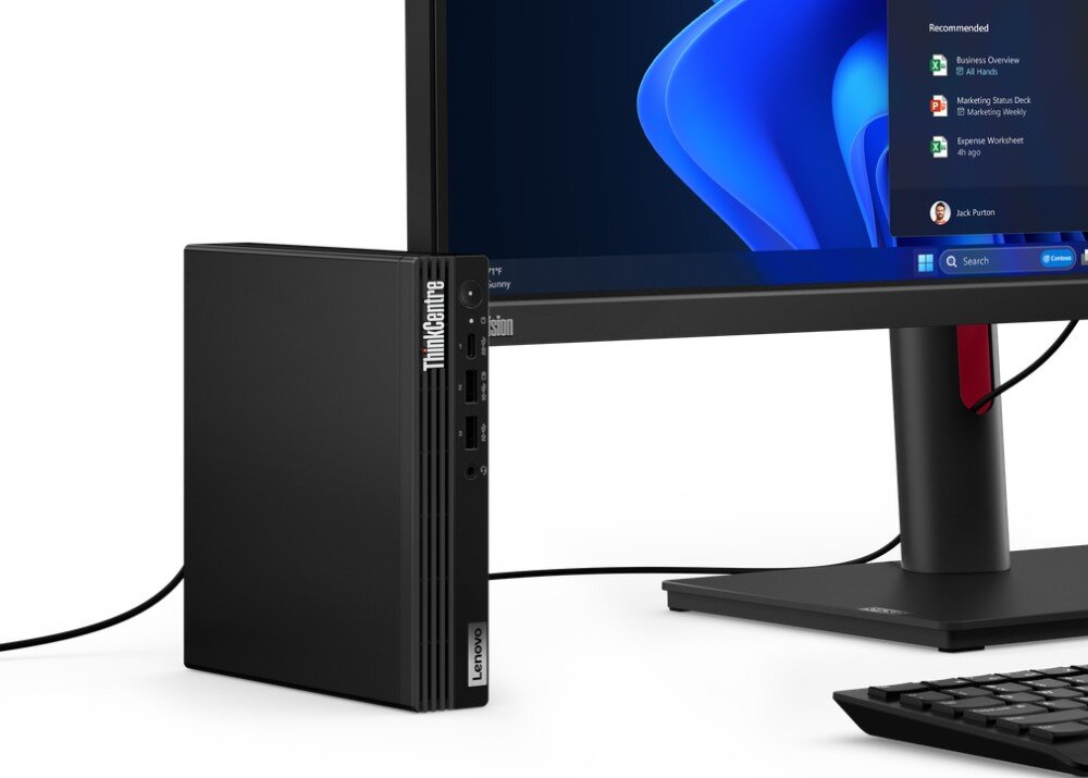 Komputer LENOVO ThinkCentre M70q Gen 5 Zbliżenie na bok monitora oraz stojącą obok niego pionowo małą czarną obudowę komputera z widocznymi portami na przednim panelu i logo producentów, dysk, interfejs, pojemność