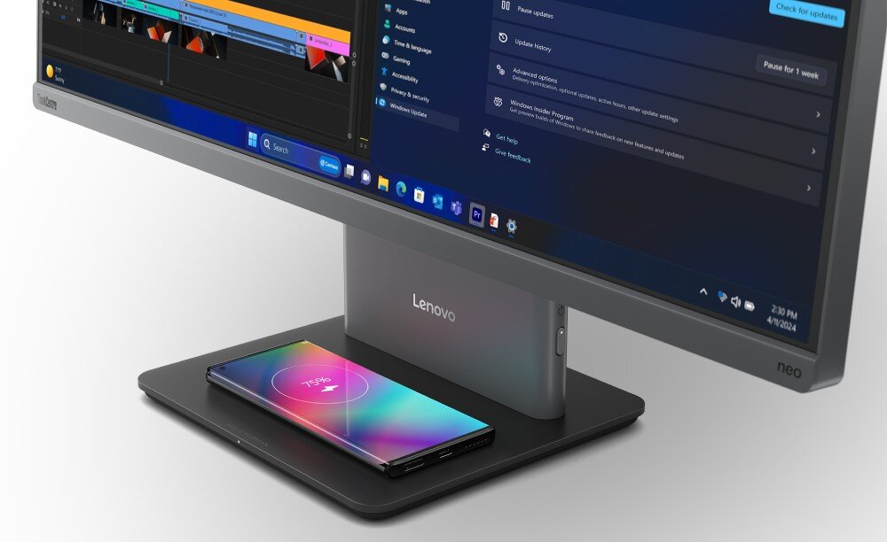 Na obrazie widoczny jest monitor z logo \'Lenovo\' na podstawie, na której leży smartfon z kolorowym ekranem. Na ekranie monitora wyświetlony jest interfejs systemu operacyjnego z ikonami aplikacji i menu ustawień.