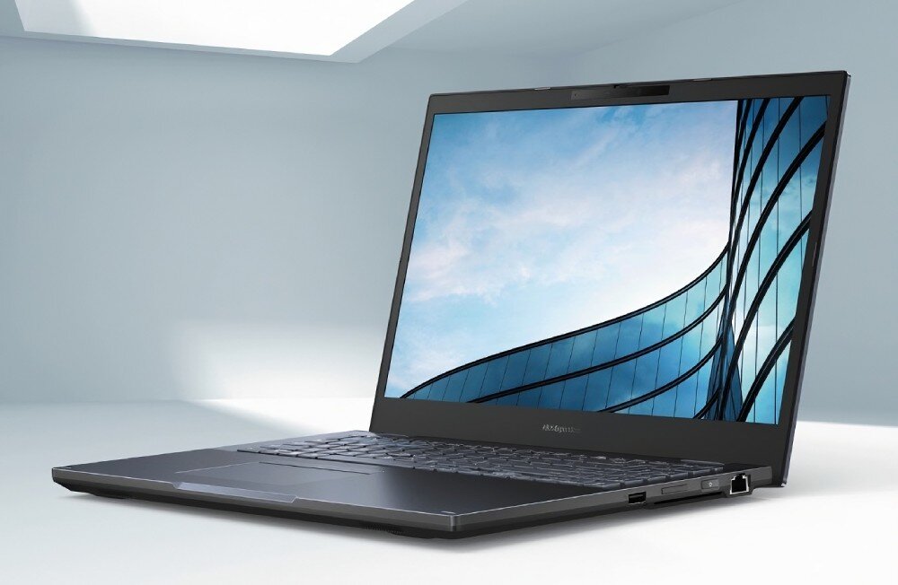 Laptop ASUS ExpertBook B2502CBA-BQ0332X Otwarty laptop na biurku, ekran wyświetla obraz nieba i przeszklonego budynku. Jasne, minimalistyczne otoczenie podkreśla jego biznesowy charakter, opis
