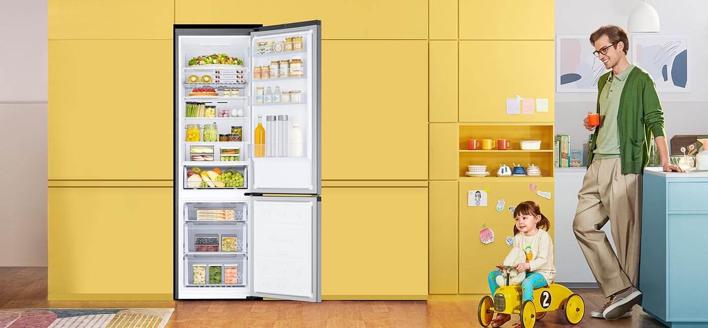 Otwarta lodówka Samsung RB38C602DSA wstawiona w żółtą zabudowę