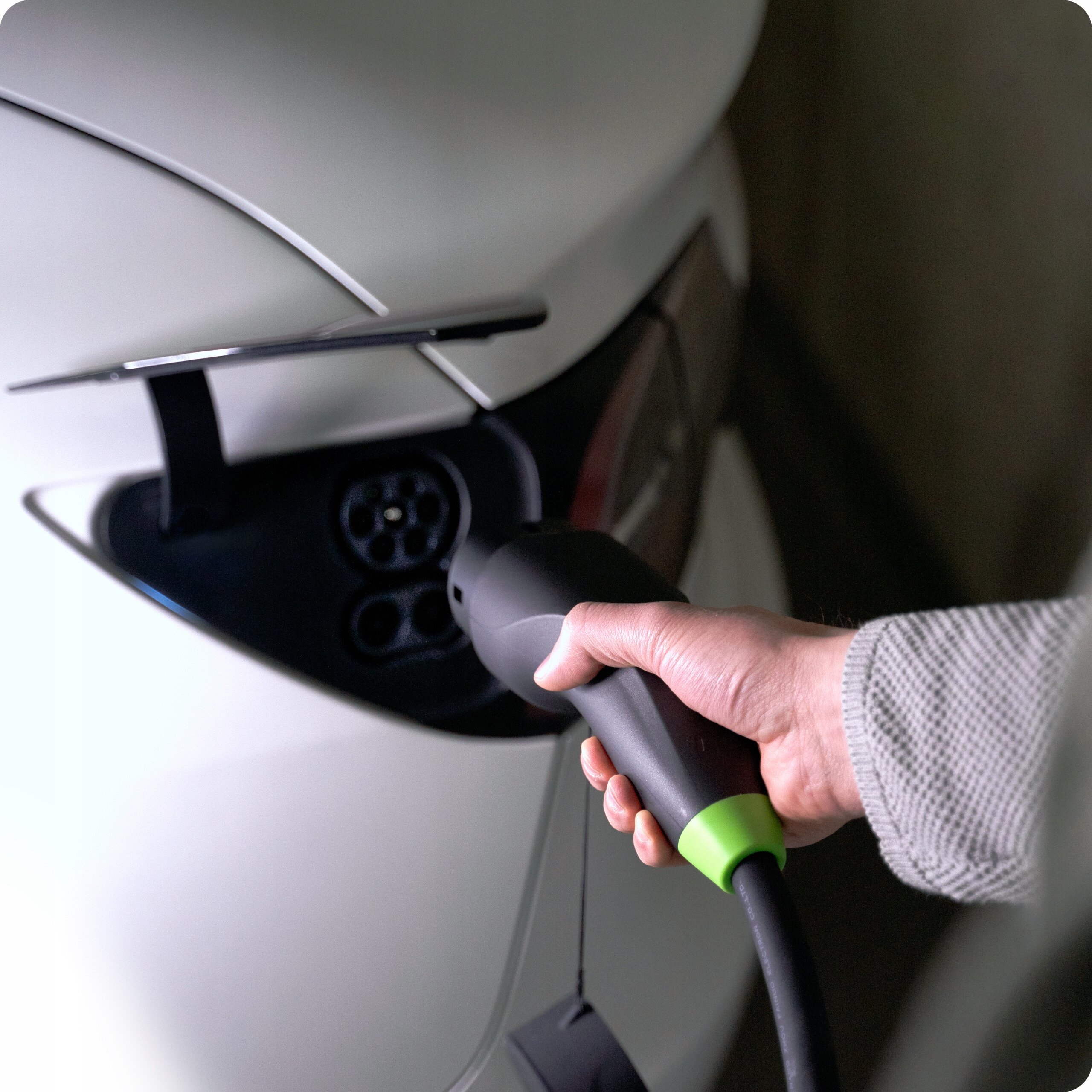 Osoba trzyma czarny kabel do ładowania z zielonym akcentem, podłączając go do gniazda ładowania samochodu elektrycznego.
