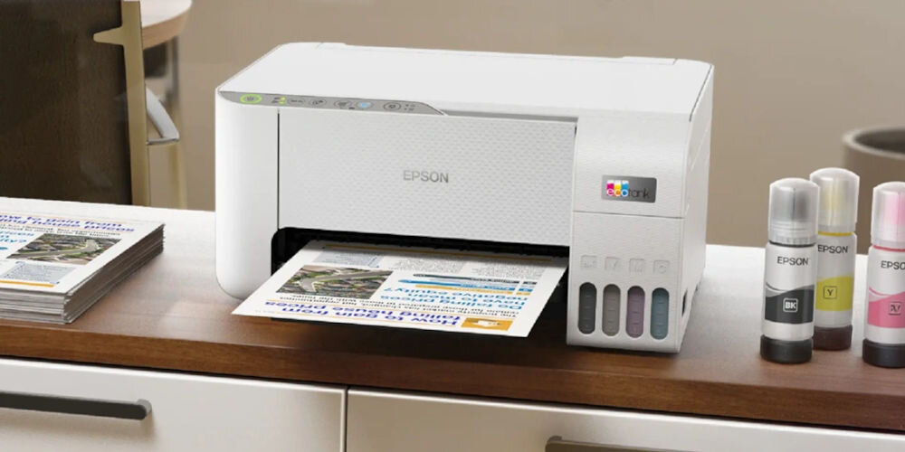 Urządzenie wielofunkcyjne EPSON EcoTank L3276 Druk w kolorze, Wi-Fi prezentacja urządzenia w pokoju na szafce obok wydrukowane już dokumenty i butelki bezkartridżowa oszczędność kosztów
