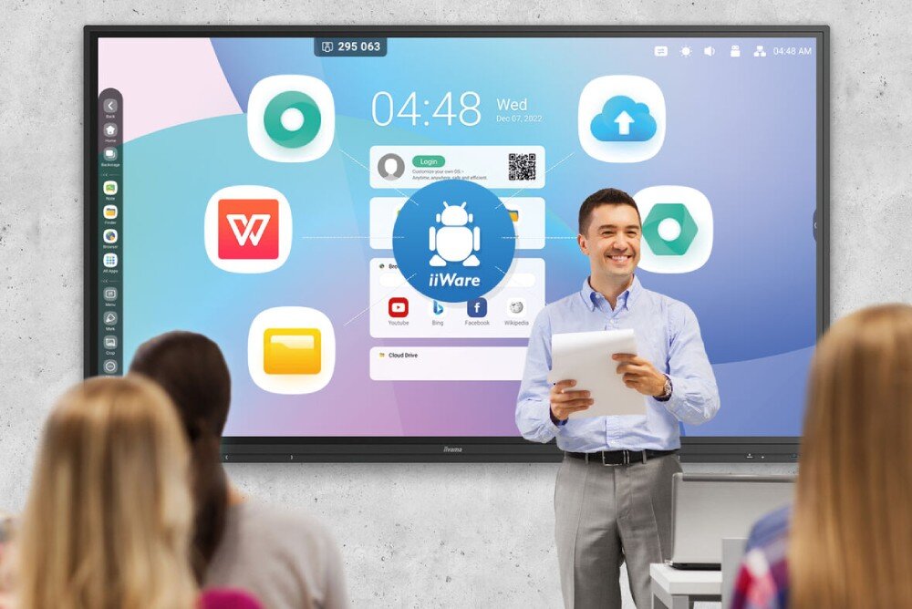 Monitor IIYAMA ProLite TE8612MIS-B3AG Mężczyzna w jasnej koszuli stoi przed dużym ekranem wyświetlającym interfejs systemu z ikonami aplikacji, podczas gdy kilka osób siedzi i patrzy na ekran, system, funkcje, aplikacje