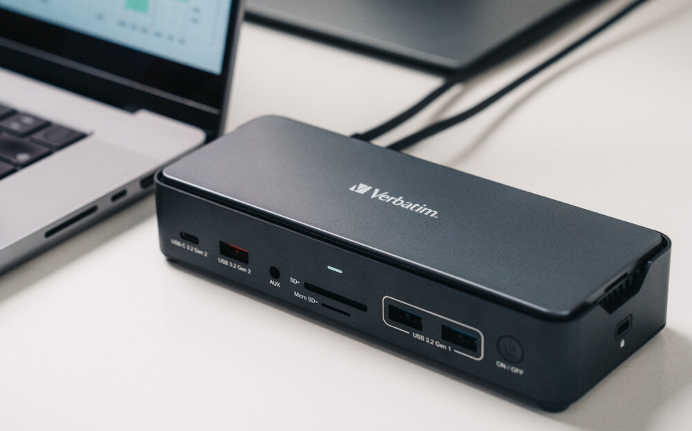 Na obrazie widoczna jest stacja dokująca z logo Verbatim, posiadająca różne porty, w tym USB 3.2 Gen 2, AUX, SD i Micro SD. Obok znajduje się fragment laptopa.