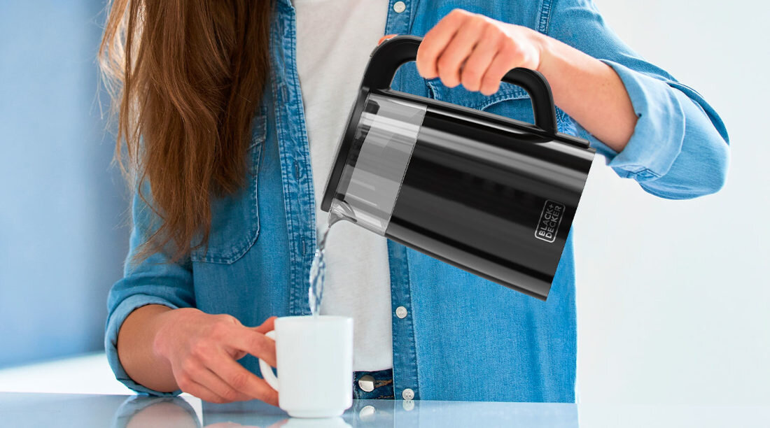 Osoba w dżinsowej koszuli nalewa wodę z czarnego czajnika do białego kubka. Na czajniku widoczne jest logo \'BLACK&DECKER\'.