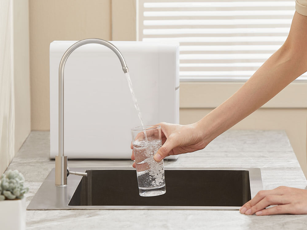 Wkład filtrujący PHILIPS AUT820/10 Kobieta nalewająca przefiltrowaną wodę z kranu PHILIPS do szklanki w nowoczesnej kuchni.