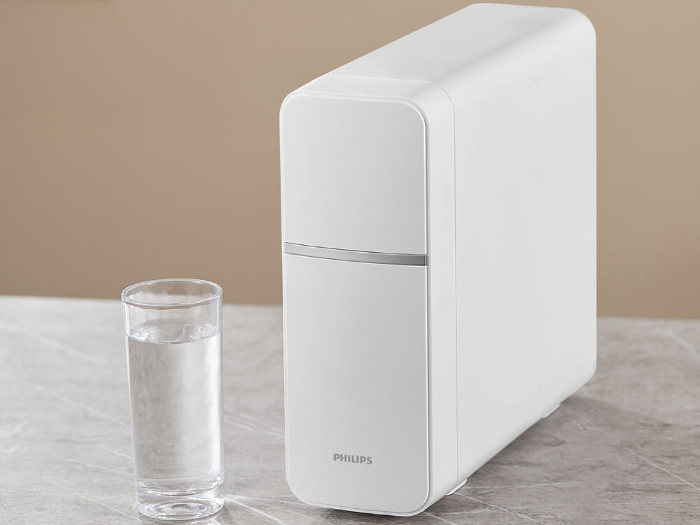 Wkład filtrujący PHILIPS AUT820/10 Biała, kompaktowa obudowa systemu filtracji wody podblatowej PHILIPS obok szklanki czystej wody.