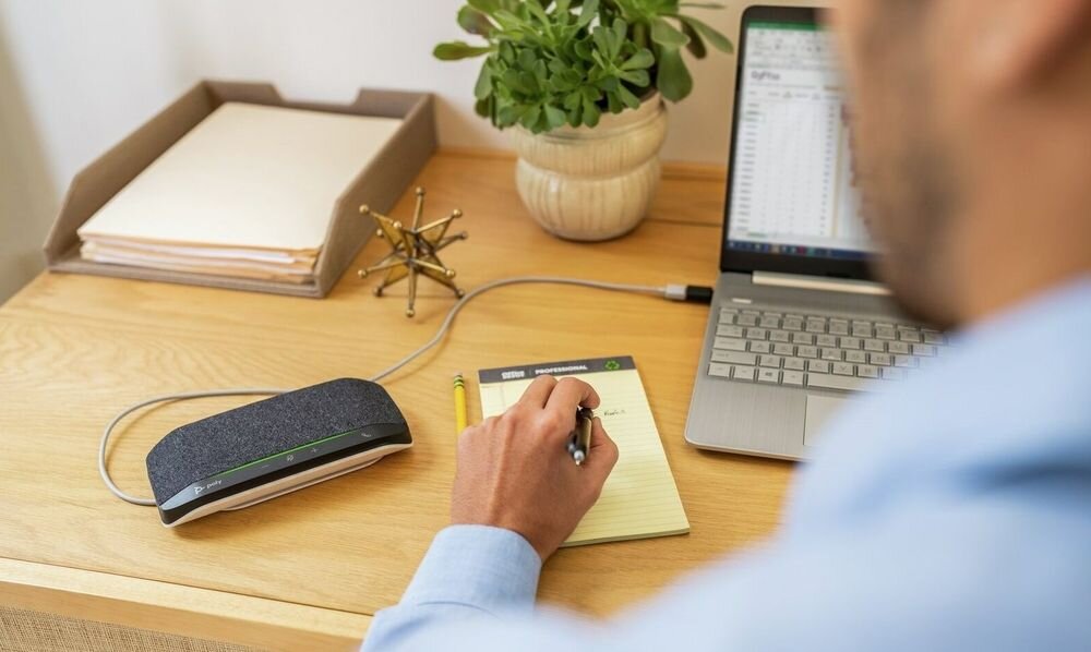 Zestaw głośnomówiący HP Poly Sync 10 profesjonalna jakość rozmów wygoda obsługa, osoba pracująca na laptopie, głośnik leżący na biurku