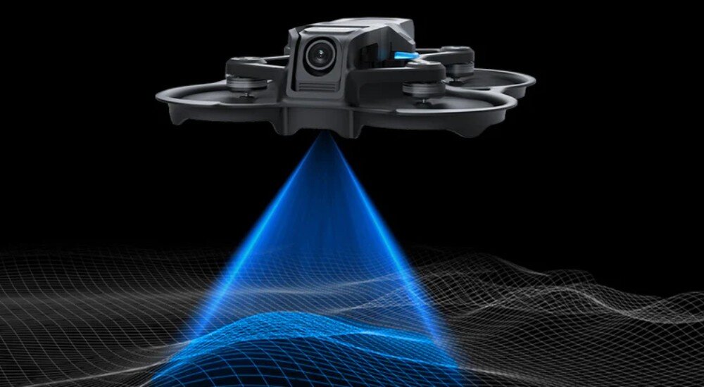 Dron BETAFPV Aquila 16 Dron zawieszony w powietrzu z niebieskim stożkiem światła skierowanym w dół na cyfrową siatkę terenu, co symbolizuje działanie czujników wysokości