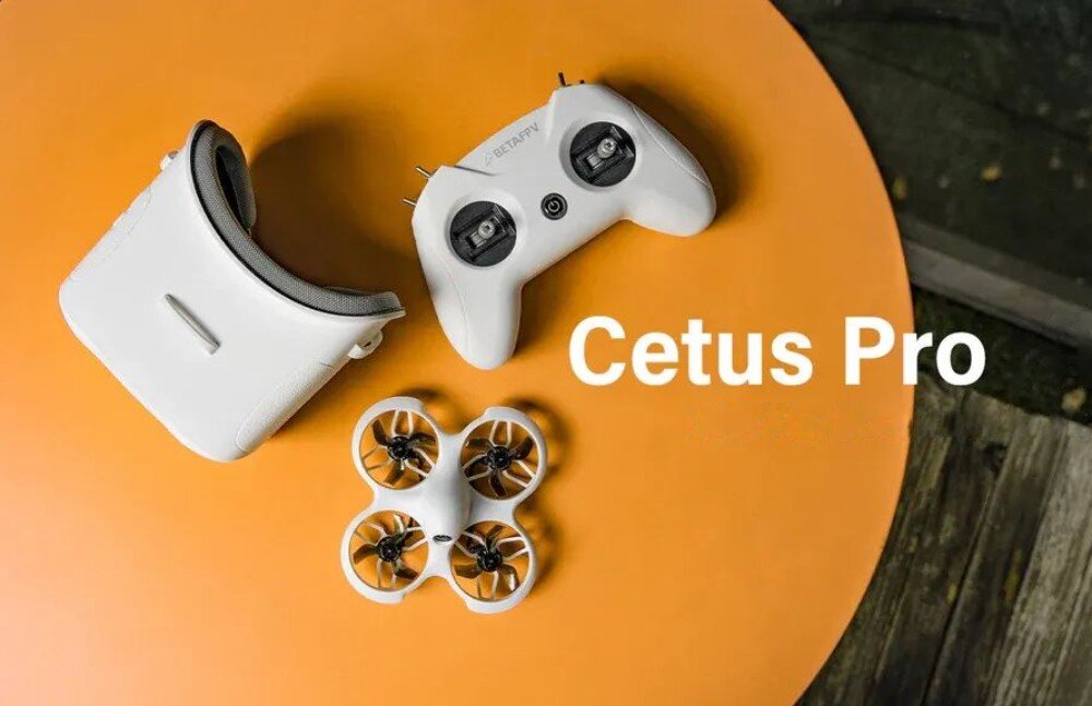 Dron BETAFPV Cetus Pro FPV Kit Zestaw składający się z gogli, aparatury sterującej i drona ułożony na pomarańczowym stole z widocznym białym napisem 'Cetus Pro'