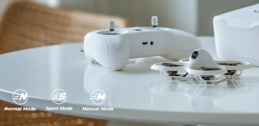 Dron BETAFPV Cetus Pro FPV Kit Dron i kontroler leżące na białym blacie z dodanymi cyfrowo w lewym rogu ikonami trybów lotu oznaczonymi literami N, S i M