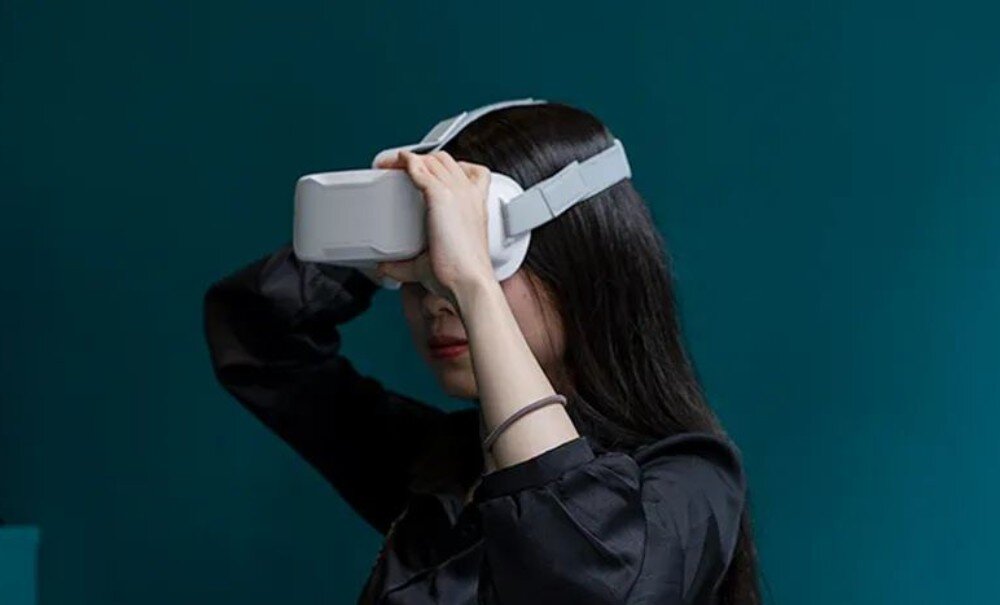 Dron BETAFPV Cetus Pro FPV Kit Osoba w czarnej koszuli trzymająca dłonie na założonych na oczy białych goglach FPV na ciemnym tle