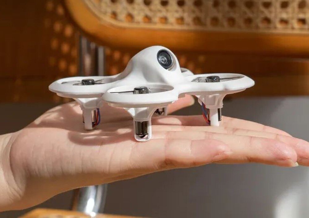 Dron BETAFPV Cetus Lite FPV Kit Dłoń trzymająca miniaturowego białego drona z czterema silnikami i centralnie umieszczoną kamerą