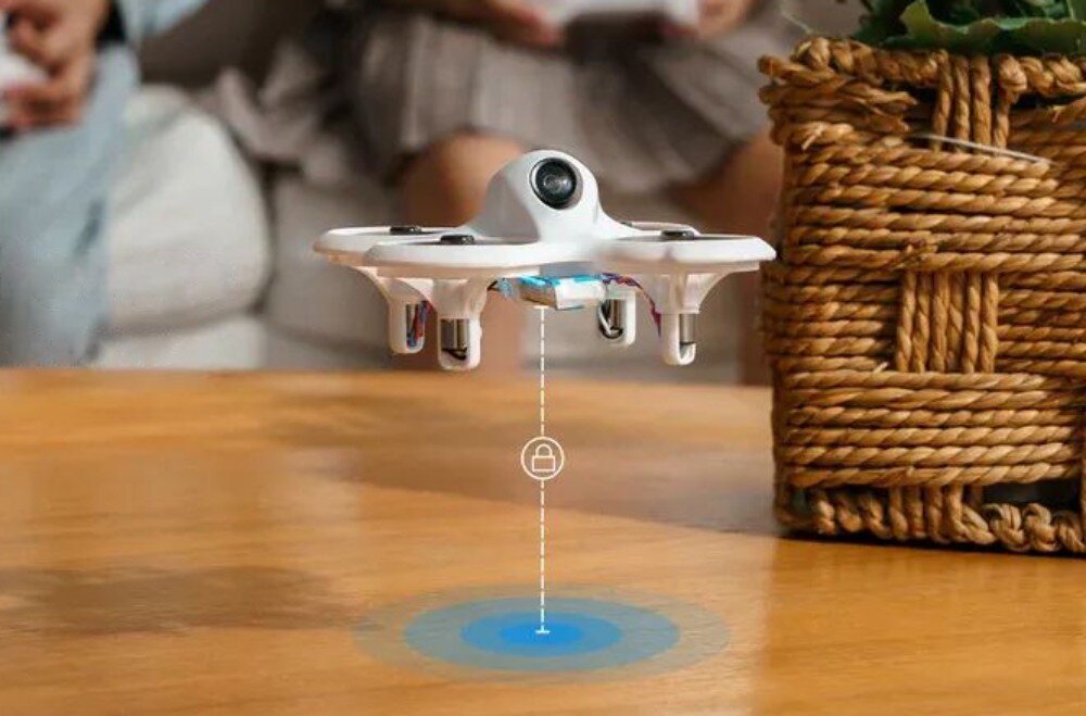 Dron BETAFPV Cetus Lite FPV Kit Biały miniaturowy dron z osłonami śmigieł unoszący się nad drewnianym blatem z wizualizacją funkcji stabilizacji wysokości