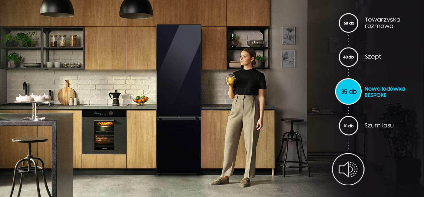 Lodówka Samsung Bespoke RB38C7B6A22 - praca na poziomie 35 dB Kuchnia z drewnianymi szafkami, w której stoi czarna lodówka. Obok kobieta trzymająca szklankę, a po prawej stronie widoczna jest grafika z poziomami hałasu, gdzie \'Nowa lodówka BESPOKE\' ma 35 dB.