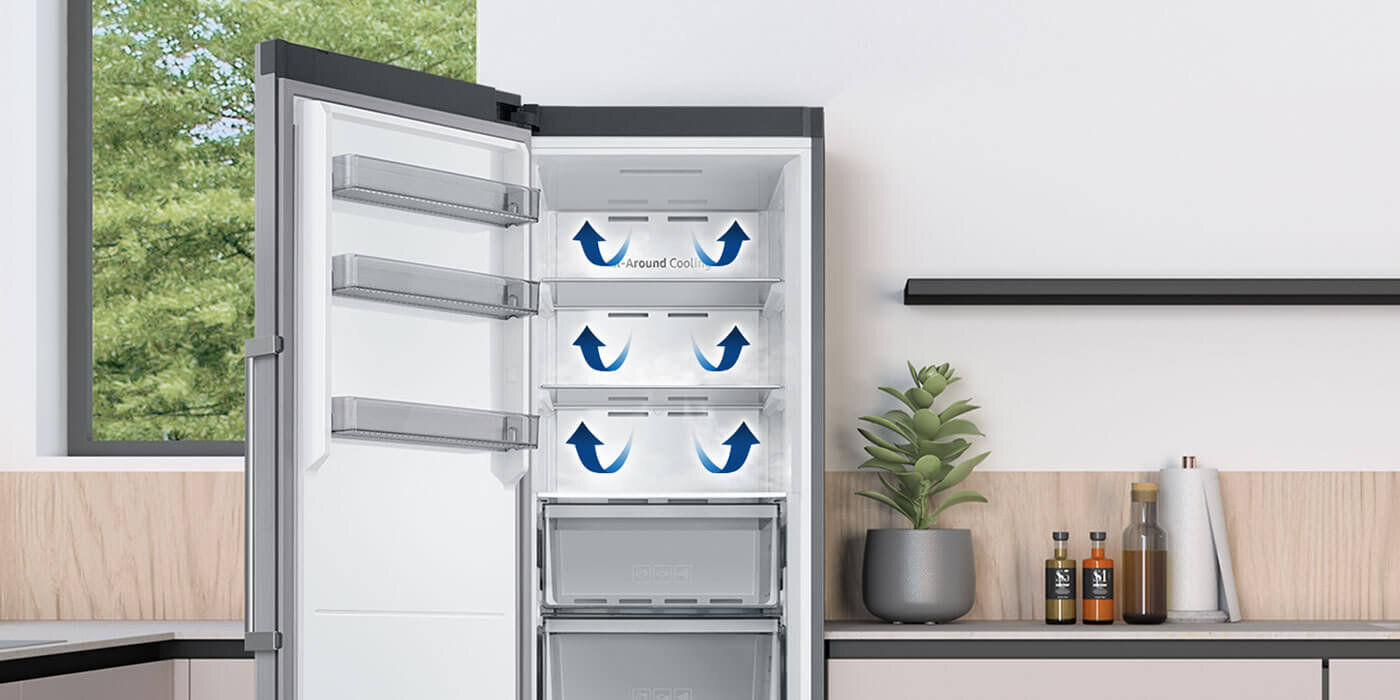 Otwarta zamrażarka z kilkoma półkami, na których widoczne są niebieskie strzałki i napis \'All-Around Cooling\'. W tle znajduje się kuchnia z rośliną doniczkową i kilkoma butelkami na blacie.