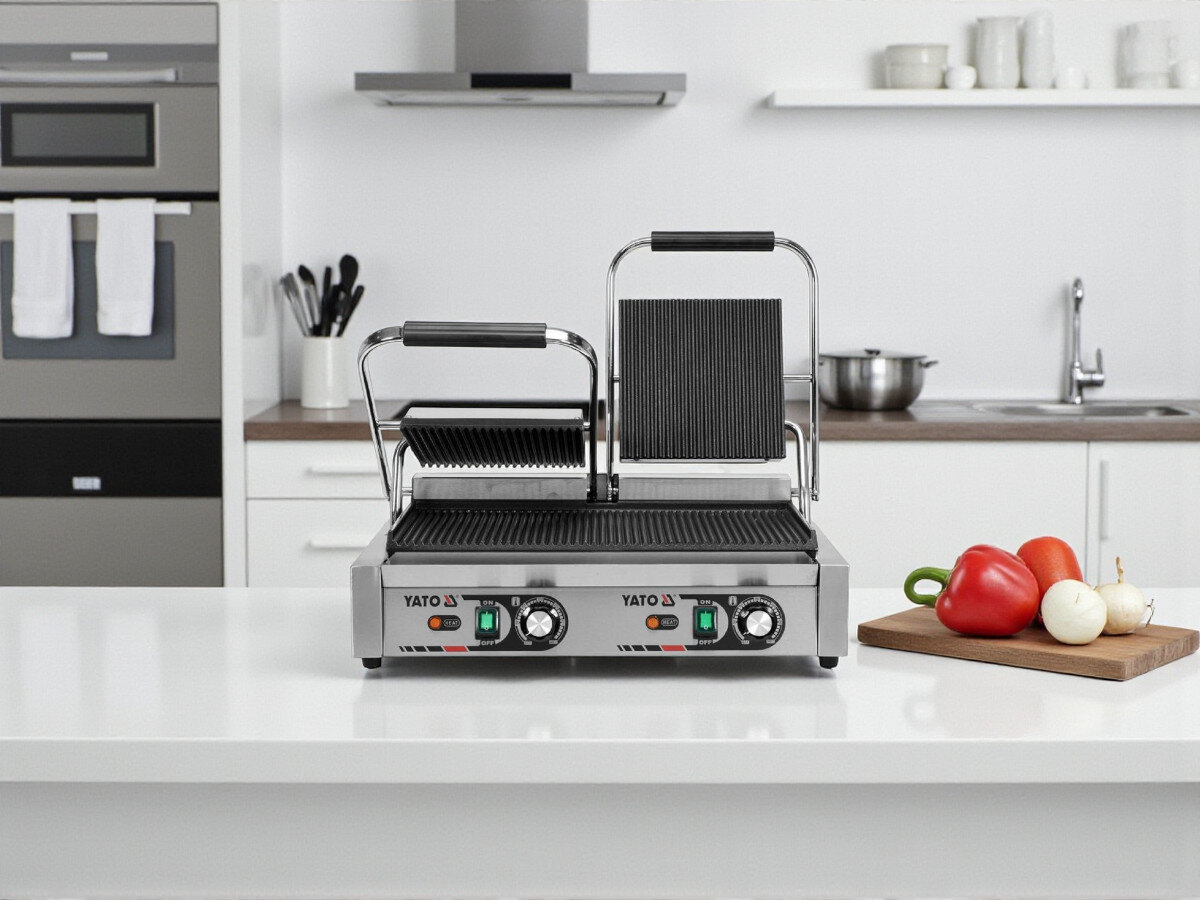 Grill elektryczny YATO YG-04560, grill, żeliwo, trzy płyty, różnorodność, Podwójny grill kontaktowy YATO YG-04560 w otwartej pozycji ustawiony na wyspie kuchennej, na blacie deska z warzywami.
